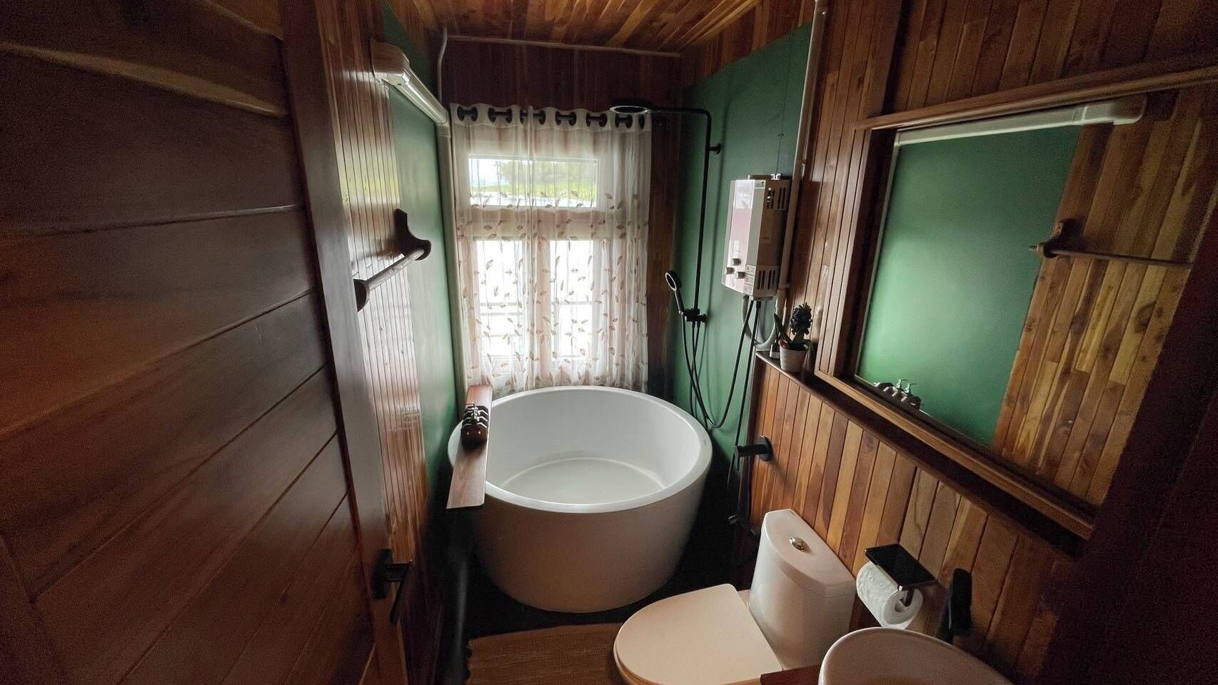 Baño de cabaña de madera con bañera independiente, inodoro y espejo.
