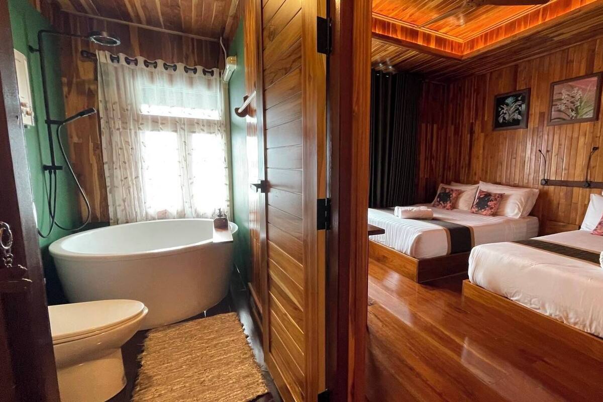 A wooden-floored room with a large bathtub, two single beds, and a toilet.