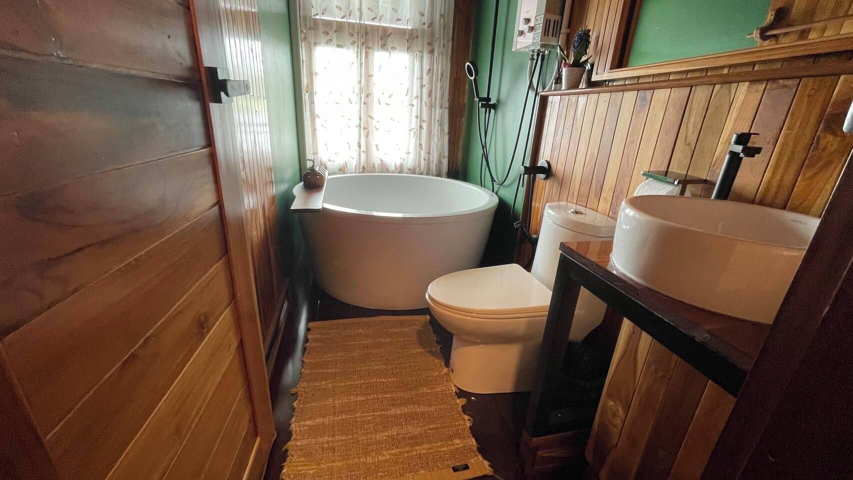 Un baño de madera con bañera, inodoro y tocador de madera con lavabo.