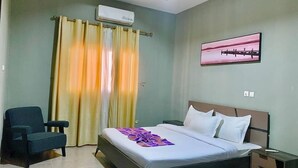 A hotel room with a bed, a chair, a nightstand, and a painting on the wall. - HAIRAI-APPART HOTEL (Korhogo)