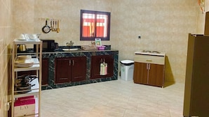 A kitchen with a marble countertop, wooden cabinets, a window with curtains, and a sink. - HAIRAI-APPART HOTEL (Korhogo)