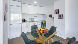 A modern kitchen with white cabinets, a glass dining table with four chairs, and a fruit bowl on the table.