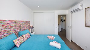 A modern hotel room with a teal bedspread, colorful headboard, and neatly arranged towels.