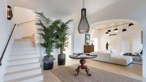 A spacious living area with a staircase, a round wooden table, and two large potted plants.
