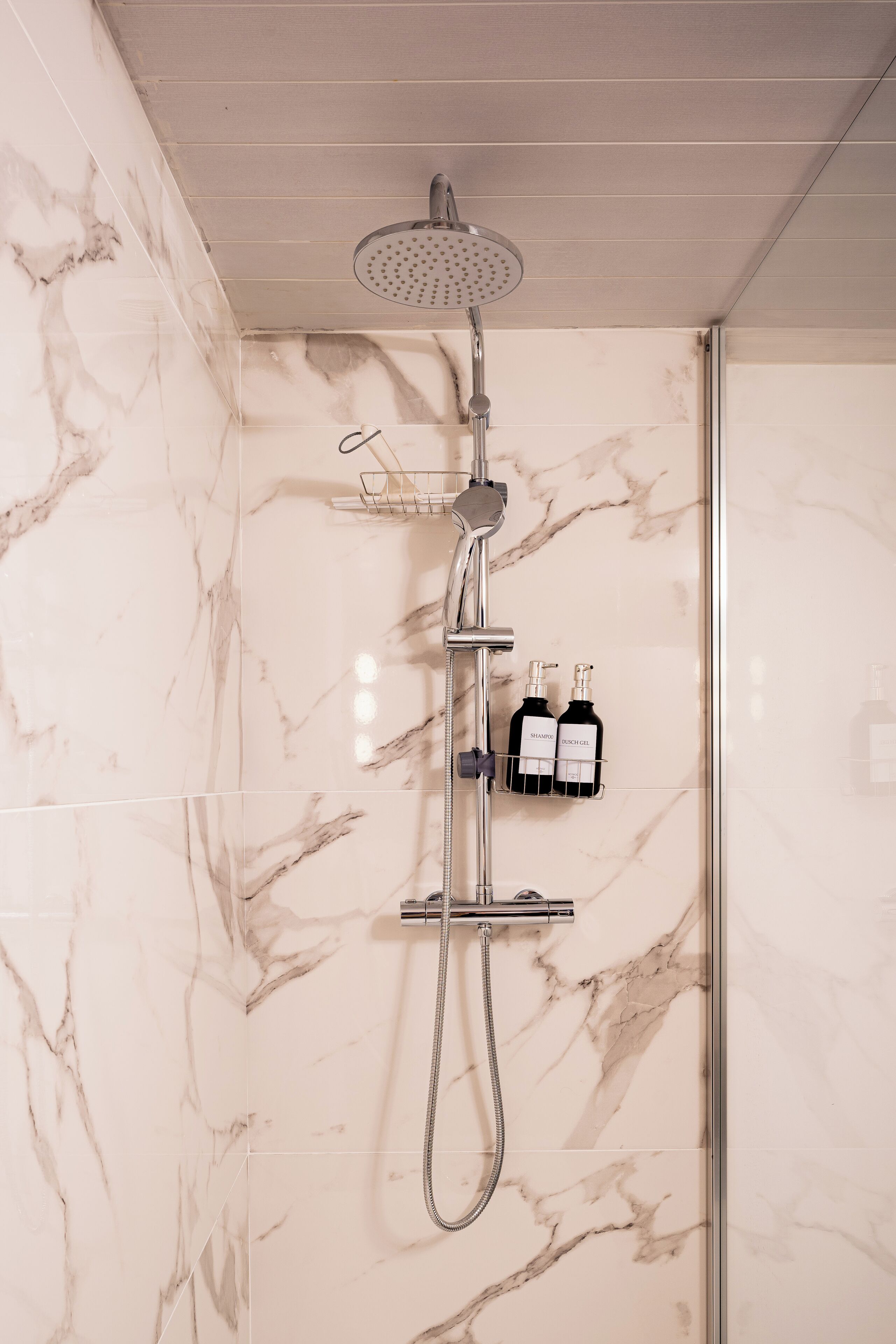 A modern bathroom with a shower, marble walls, and a towel rack with two bottles.