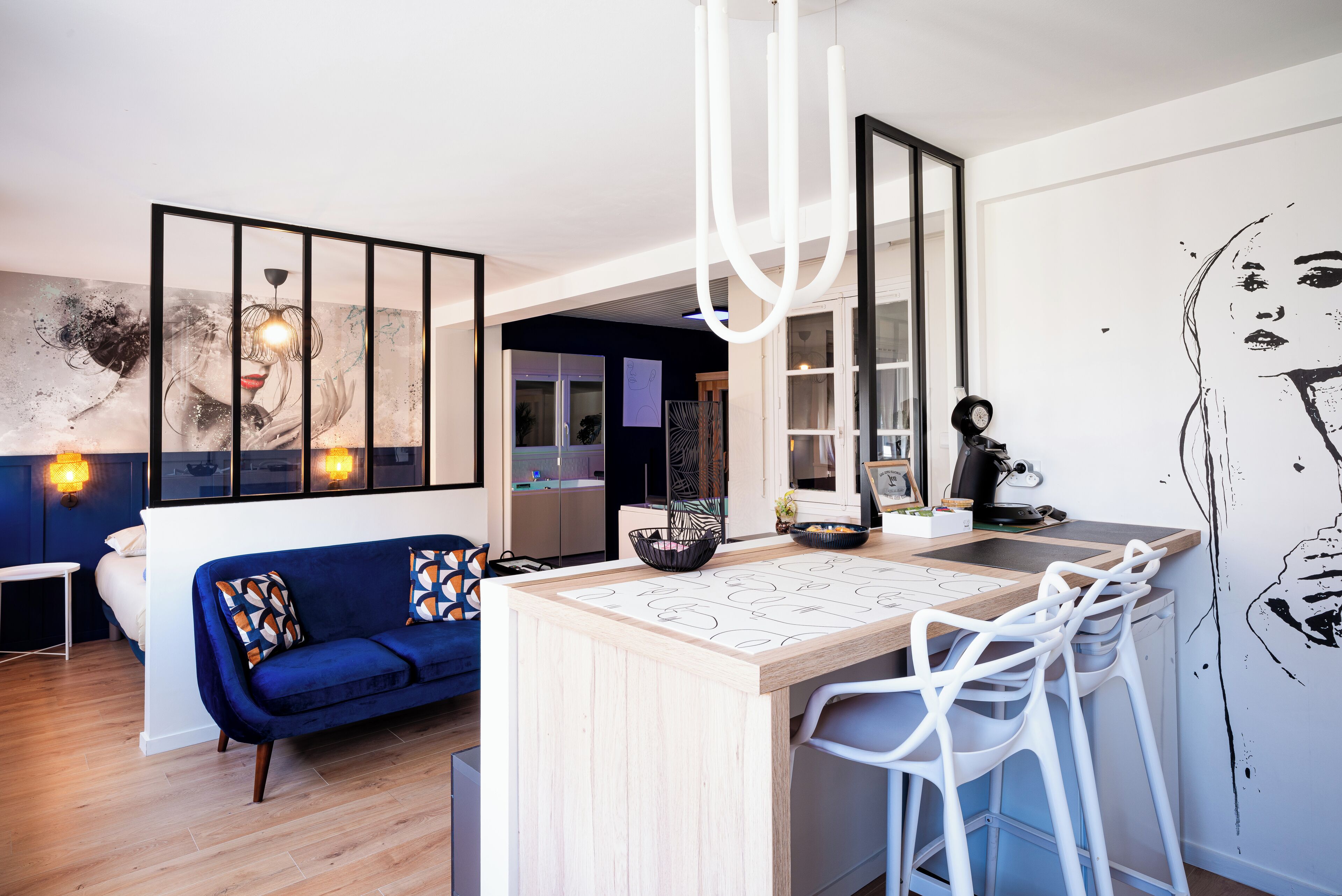 A modern living space with a central island, a blue sofa, and a kitchen area with bar stools.