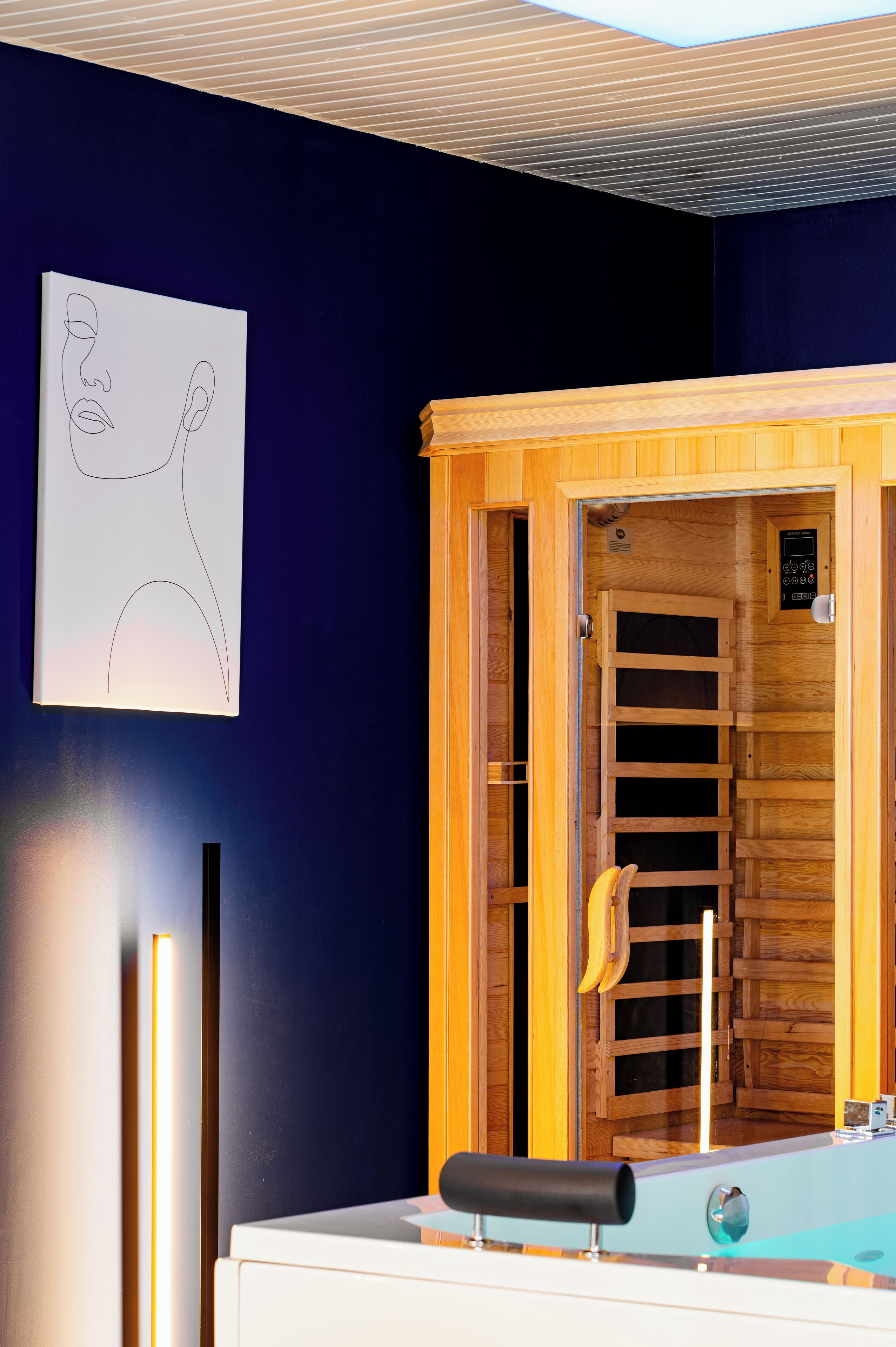 Un sauna avec une porte en bois, un panneau de commande et une œuvre d’art fixée au mur.