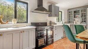 Een moderne keuken met witte kastjes, een zwarte kookplaat en een eethoek met een groene stoel.