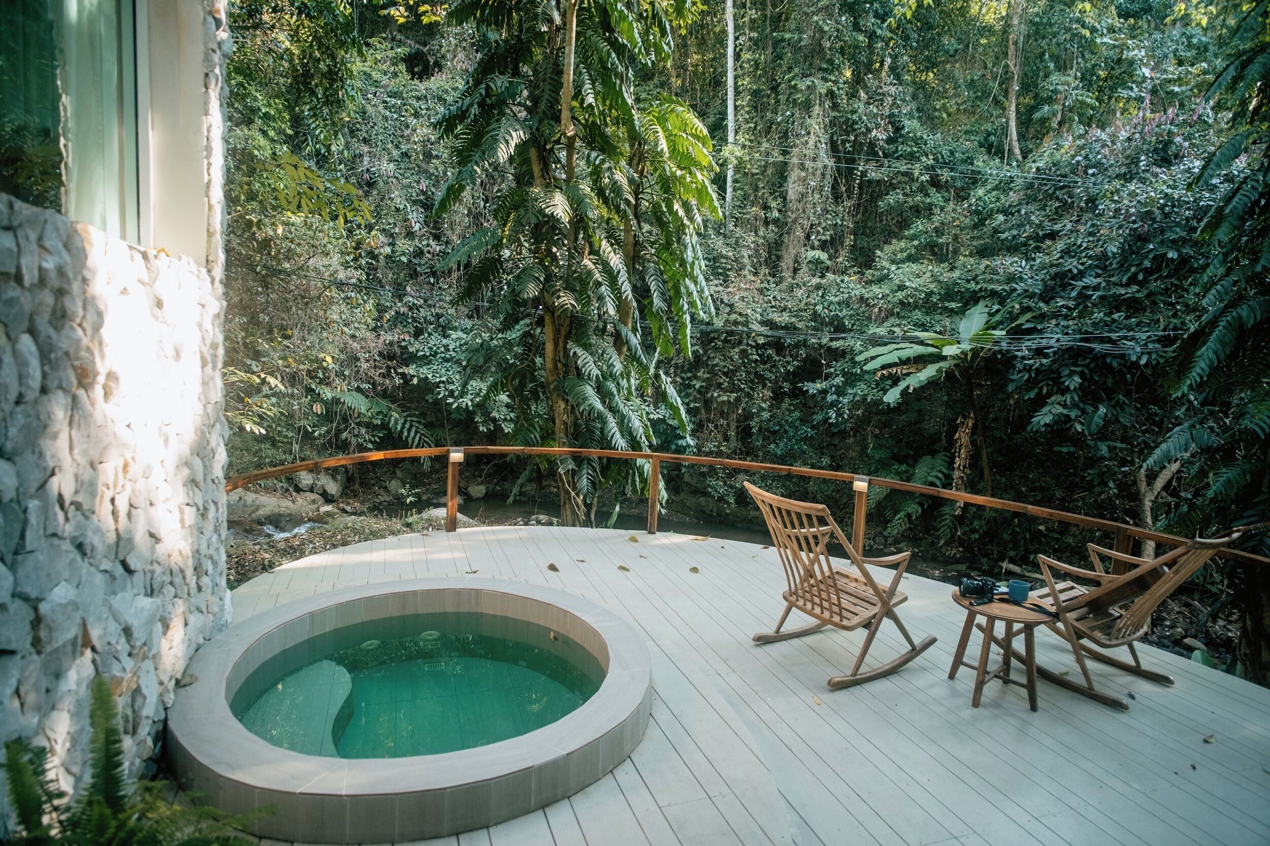 A deck with a hot tub, wooden rocking chairs, and a stone wall.