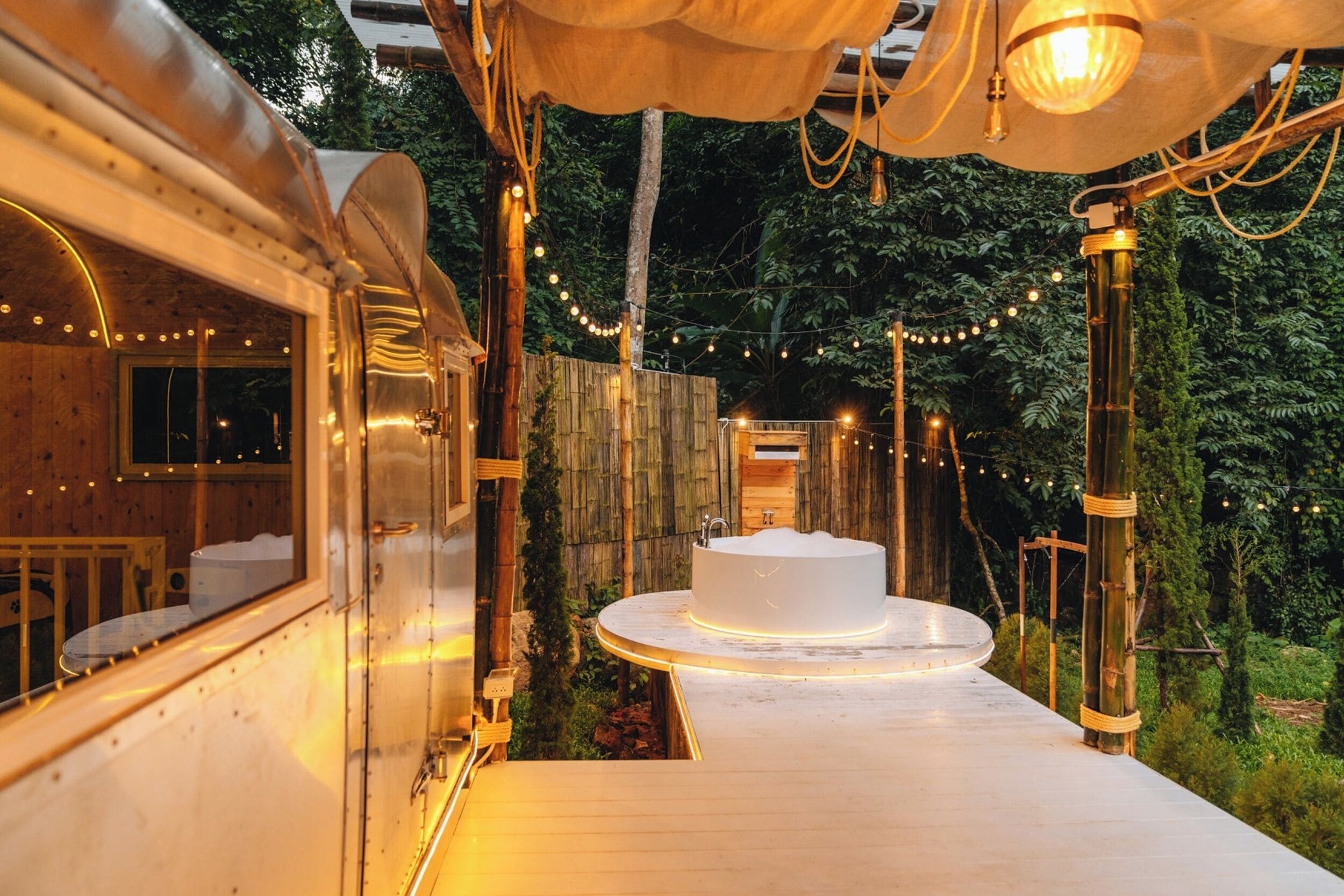 Una cabaña de madera con un balcón circular de madera, una bañera blanca y luces colgantes.