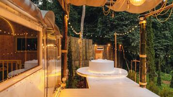Una cabaña de madera con un balcón circular de madera, una bañera blanca y luces colgantes.