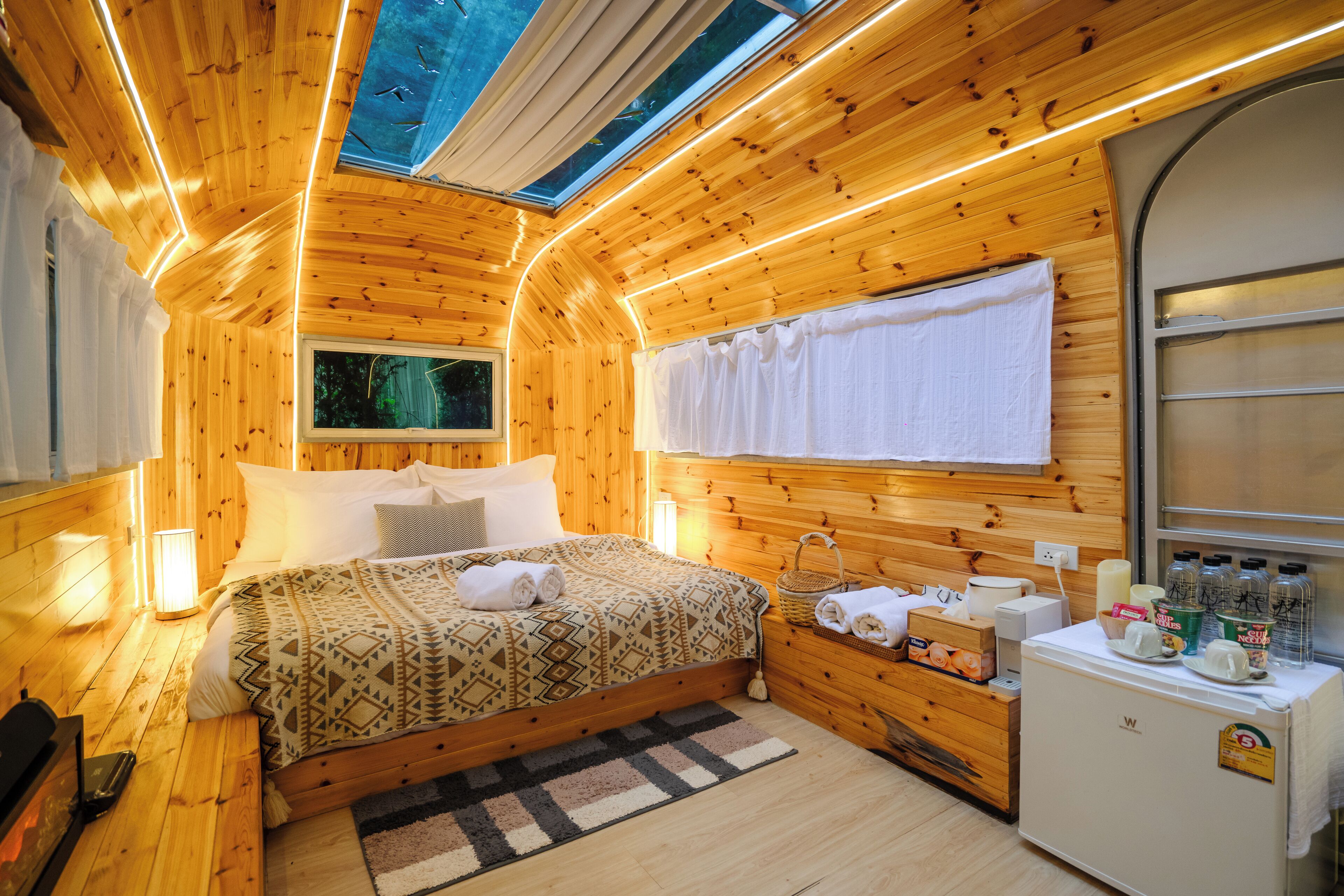 Una habitación de cabaña de madera con una cama, un refrigerador pequeño y una ventana.