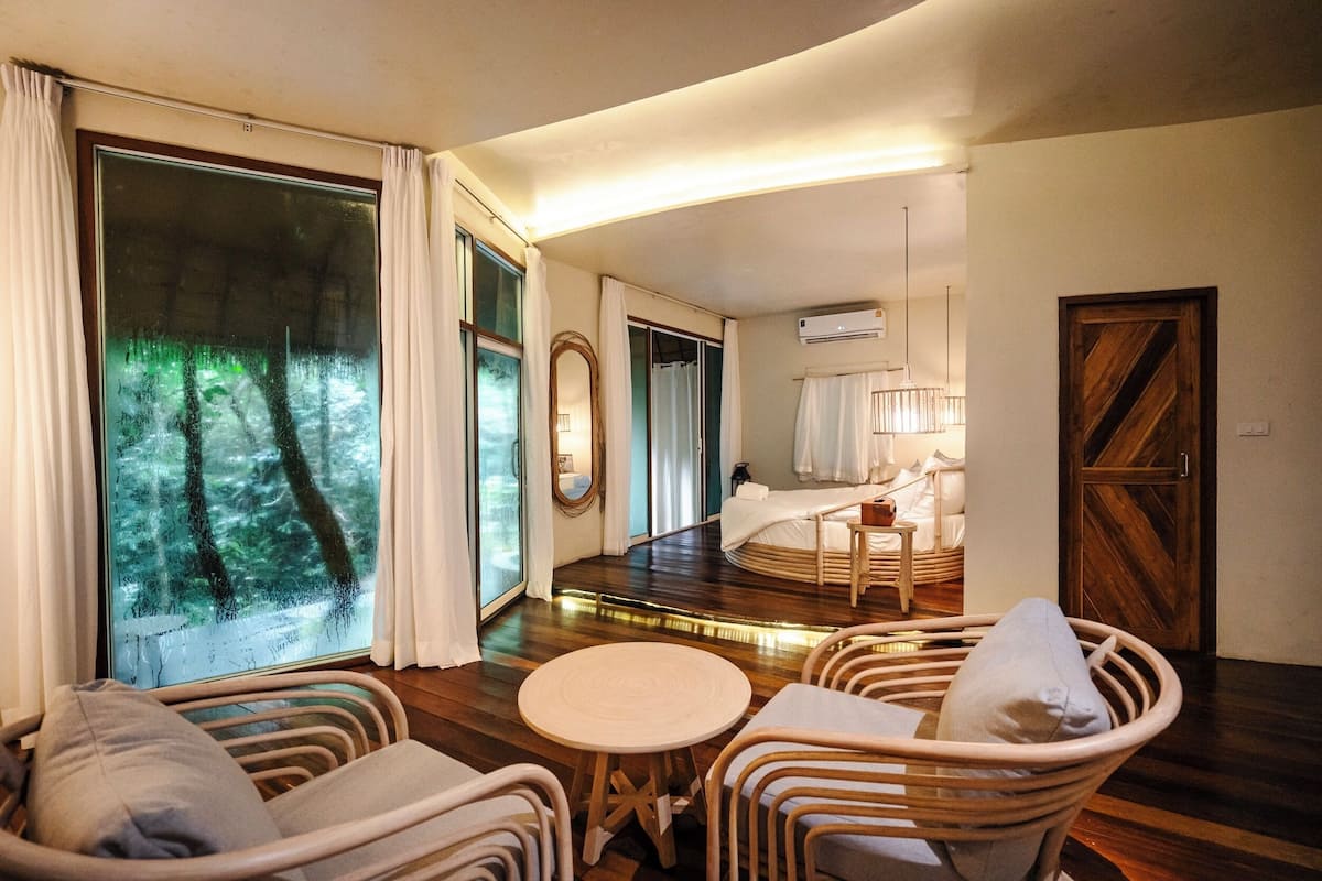 A hotel room with a large window, a bed, a round table, and wicker furniture.