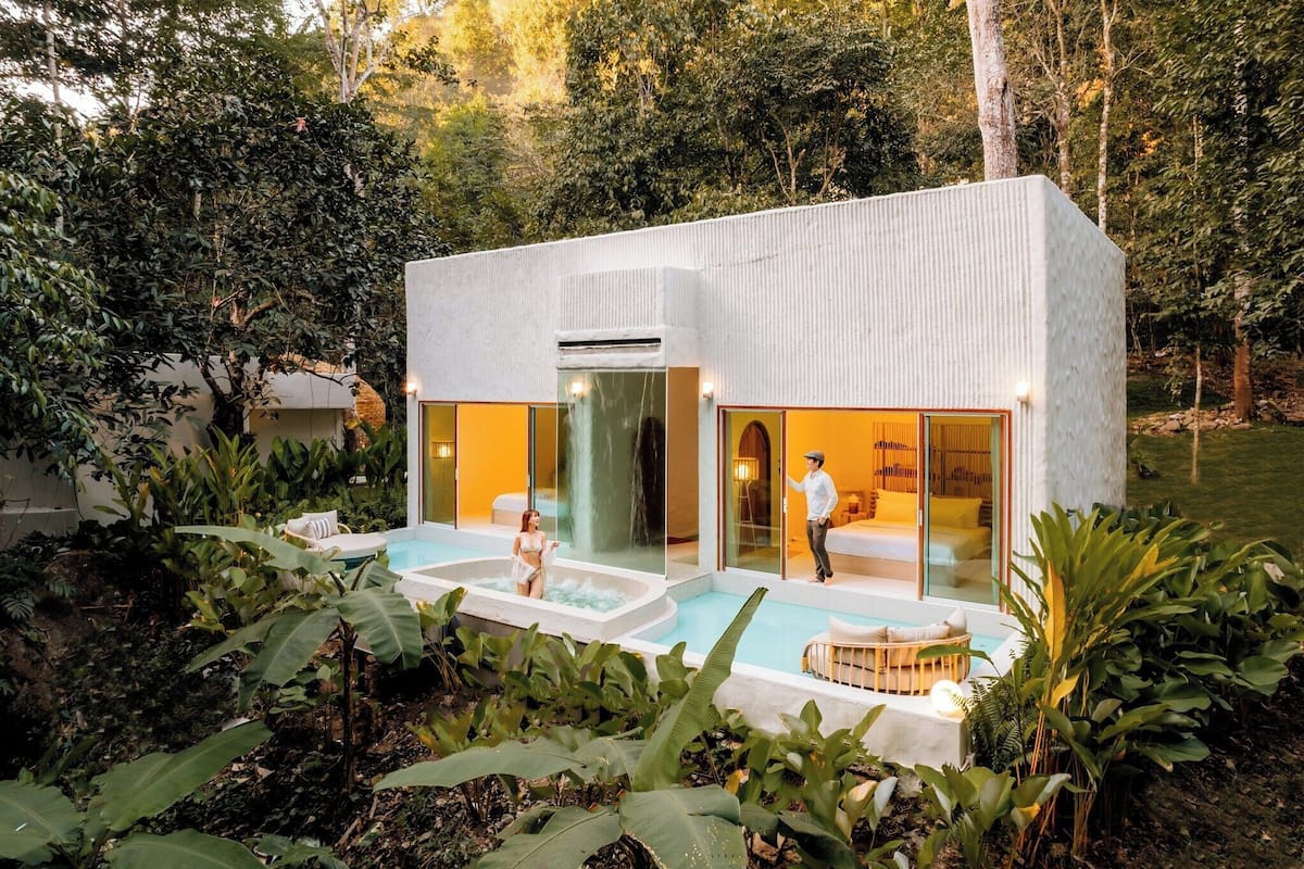 A modern house with a glass facade, a pool, and lush greenery.