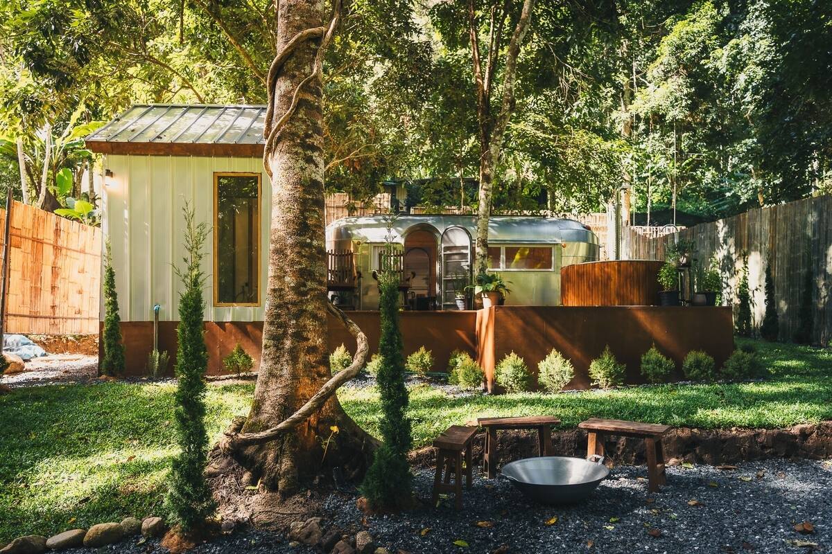 A rustic cabin with a metal roof, surrounded by a wooden fence and lush greenery.