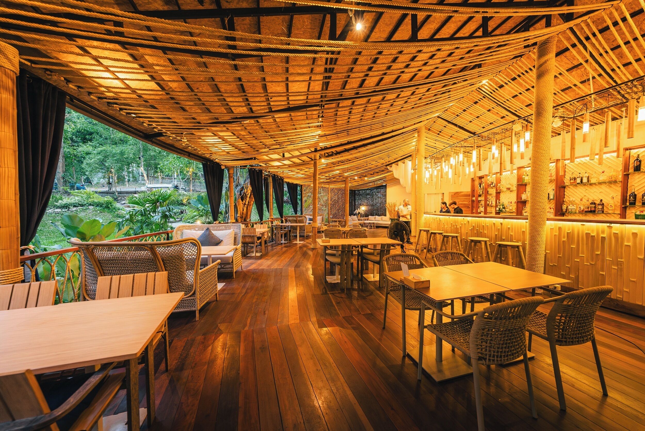 An indoor restaurant with wooden flooring, wicker furniture, and a bar area.