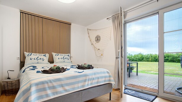 A bedroom with a bed, a bedside table, a window with a view, and a door leading to an outdoor area.