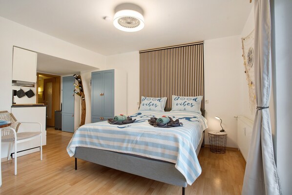 Une chambre à coucher comprenant un lit, une chaise, une petite table, une table de chevet et une étagère fixée au mur.