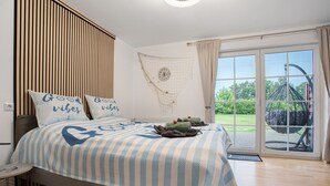 A bedroom with a bed, pillows, a wall clock, and a view of a garden through a glass door.