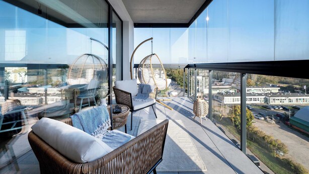 Un balcone con mobili in vimini, una sedia sospesa e vista sulla città.