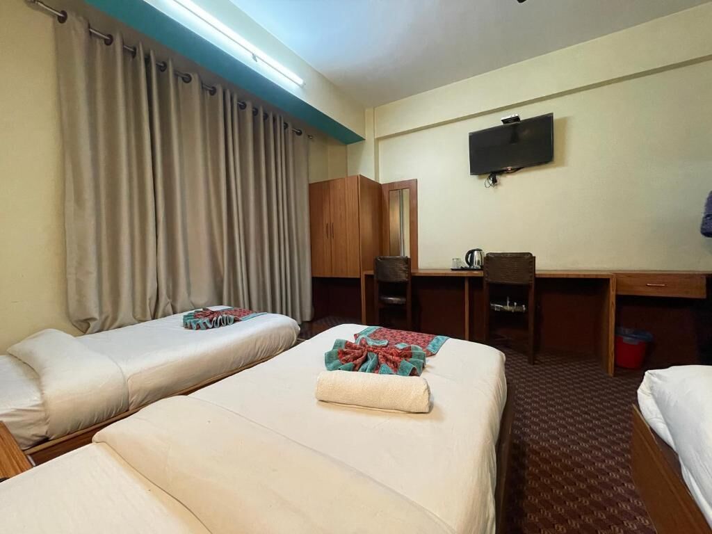 A hotel room with two beds, a desk, a chair, a television, and a wardrobe.