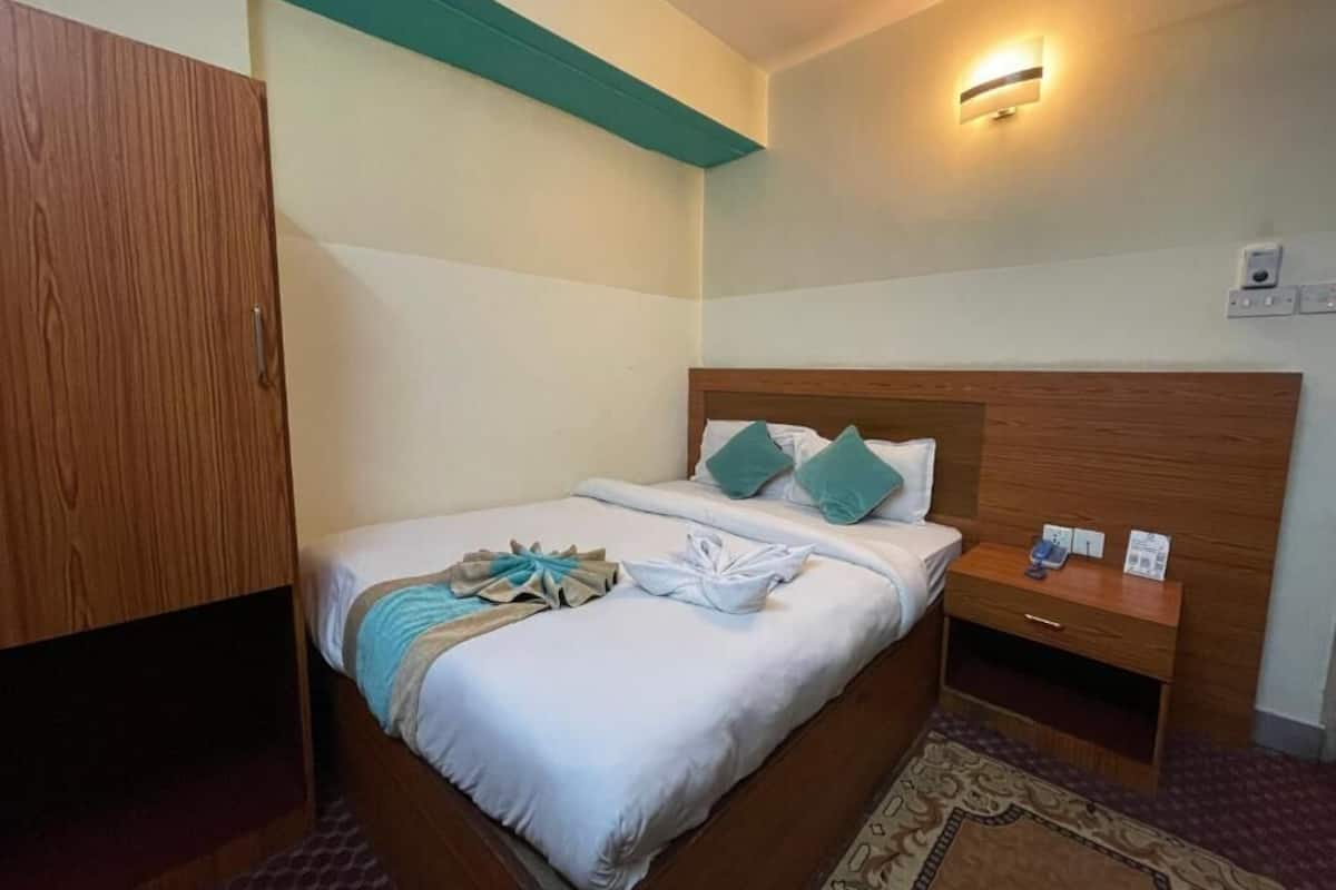 A hotel room with a wooden bed, a nightstand, a wardrobe, and a wall-mounted light fixture.
