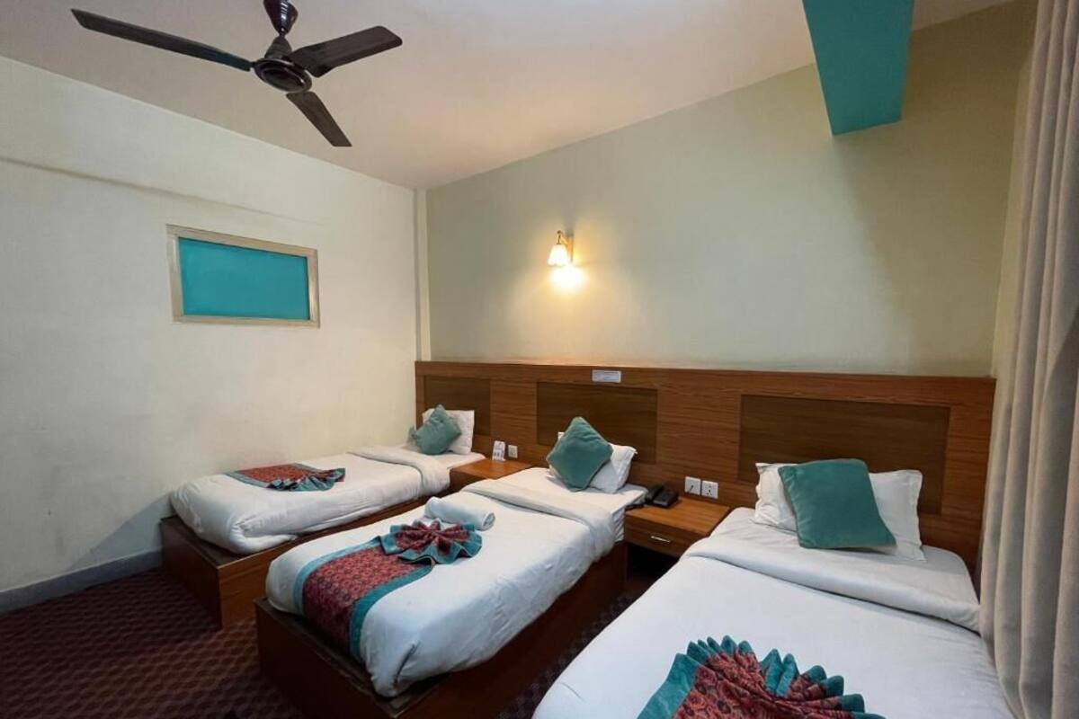 A hotel room with three single beds, a ceiling fan, a nightstand, and a wall-mounted light fixture.