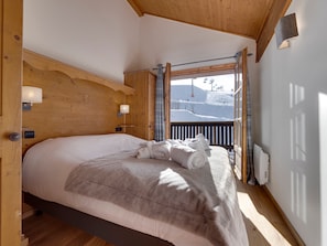 A cozy bedroom with a large bed, wooden headboard, and a view of a snowy mountain.