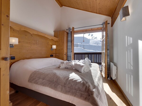 A cozy bedroom with a large bed, wooden headboard, and a view of a snowy mountain. - Arc 1950 - Spacious apt for 10 pax, 4 bedrooms, ski-in/ski-out access (Les Arcs 1950)