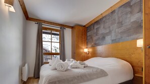 Een moderne hotelkamer met een groot bed, een houten hoofdeinde en uitzicht op een besneeerd landschap door het raam.