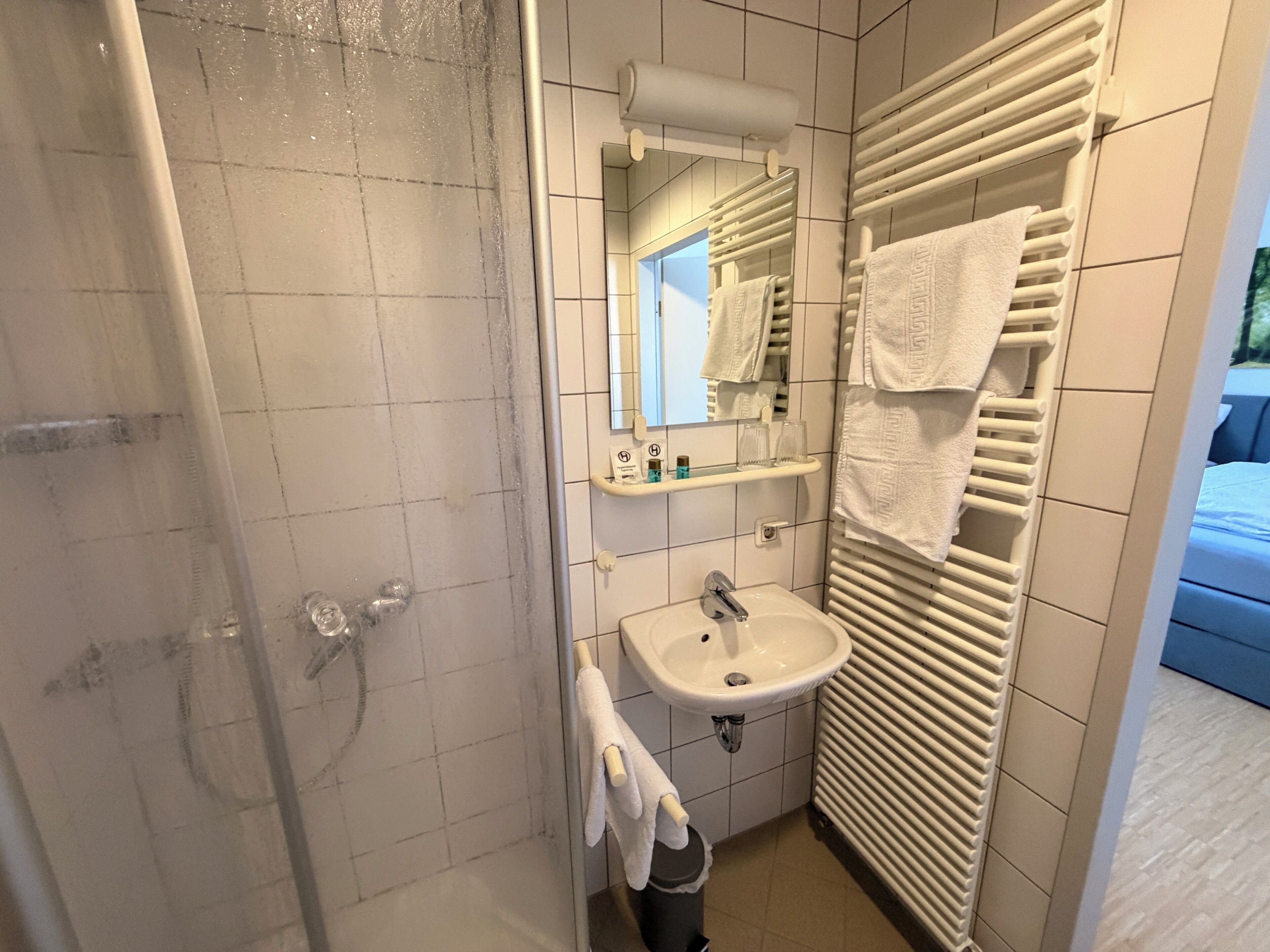 A bathroom with a shower, sink, towel rack, and a mirror.