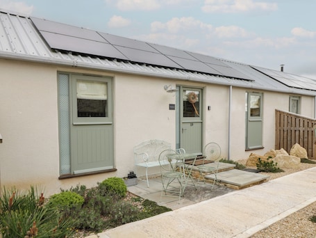 A single-story building with a green door, a small porch with a metal chair, and a solar panel roof.