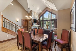 Un espace repas avec une table et des chaises en bois, un mur décoratif en pierre et une vue dégagée grâce à de grandes fenêtres.