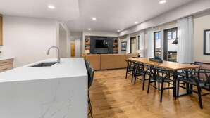A modern kitchen with a marble countertop, wooden flooring, and a dining area with a wooden table and chairs. - Moose Chalet | Exclusive Tamarack Perks (Tamarack)