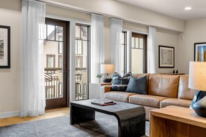A modern living room with a leather sofa, a coffee table, and a view of a balcony.