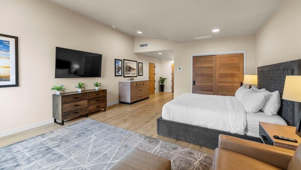 A spacious bedroom with a large bed, a TV mounted on the wall, a wooden wardrobe, and a desk with a lamp. - Moose Chalet | Exclusive Tamarack Perks (Tamarack)