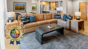 A modern living room with a sectional sofa, a coffee table, and a dining area with a table and chairs. - Moose Chalet | Exclusive Tamarack Perks (Tamarack)