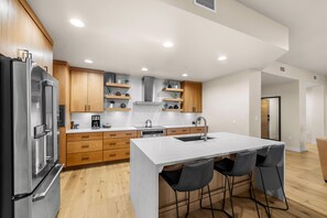 A modern kitchen with wooden cabinets, a stainless steel refrigerator, a built-in oven, a coffee maker, and a sink. - Moose Chalet | Exclusive Tamarack Perks (Tamarack)