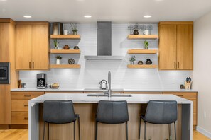 Een moderne keuken met houten kasten, een centraal eiland met barstoelen en inbouwplanken met decoratieve objecten.