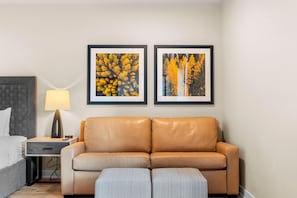 A hotel room with a bed, a nightstand with a lamp, a sofa, and two framed pictures on the wall.