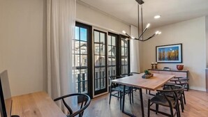 A dining area with a wooden table and chairs, large windows with black frames, and a modern pendant light.
