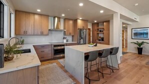 A modern kitchen with wooden cabinets, a central island, and a dining area with bar stools.