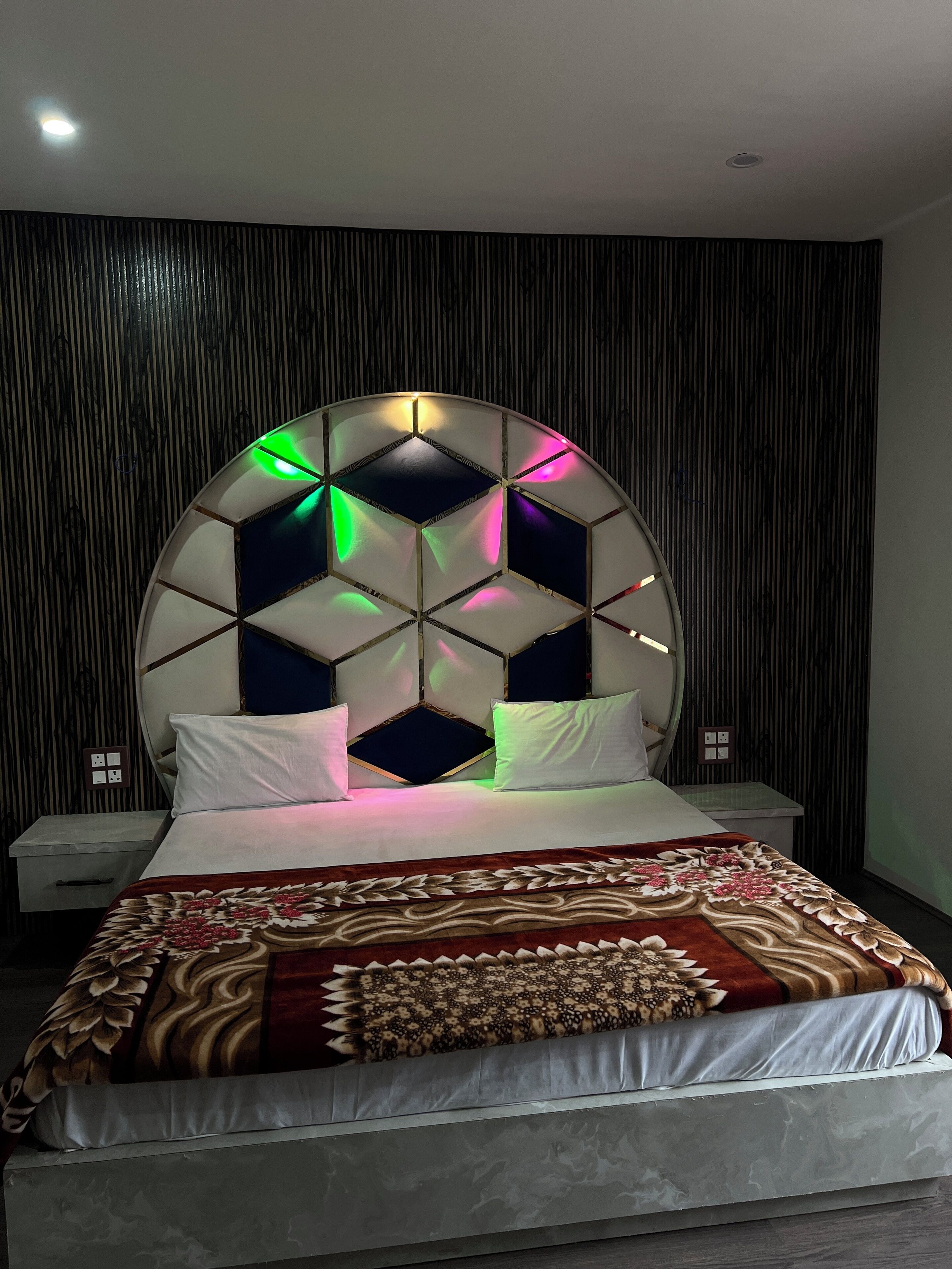 Un dormitorio moderno con cabecera geométrica, colcha estampada y mesita de noche con cajón.