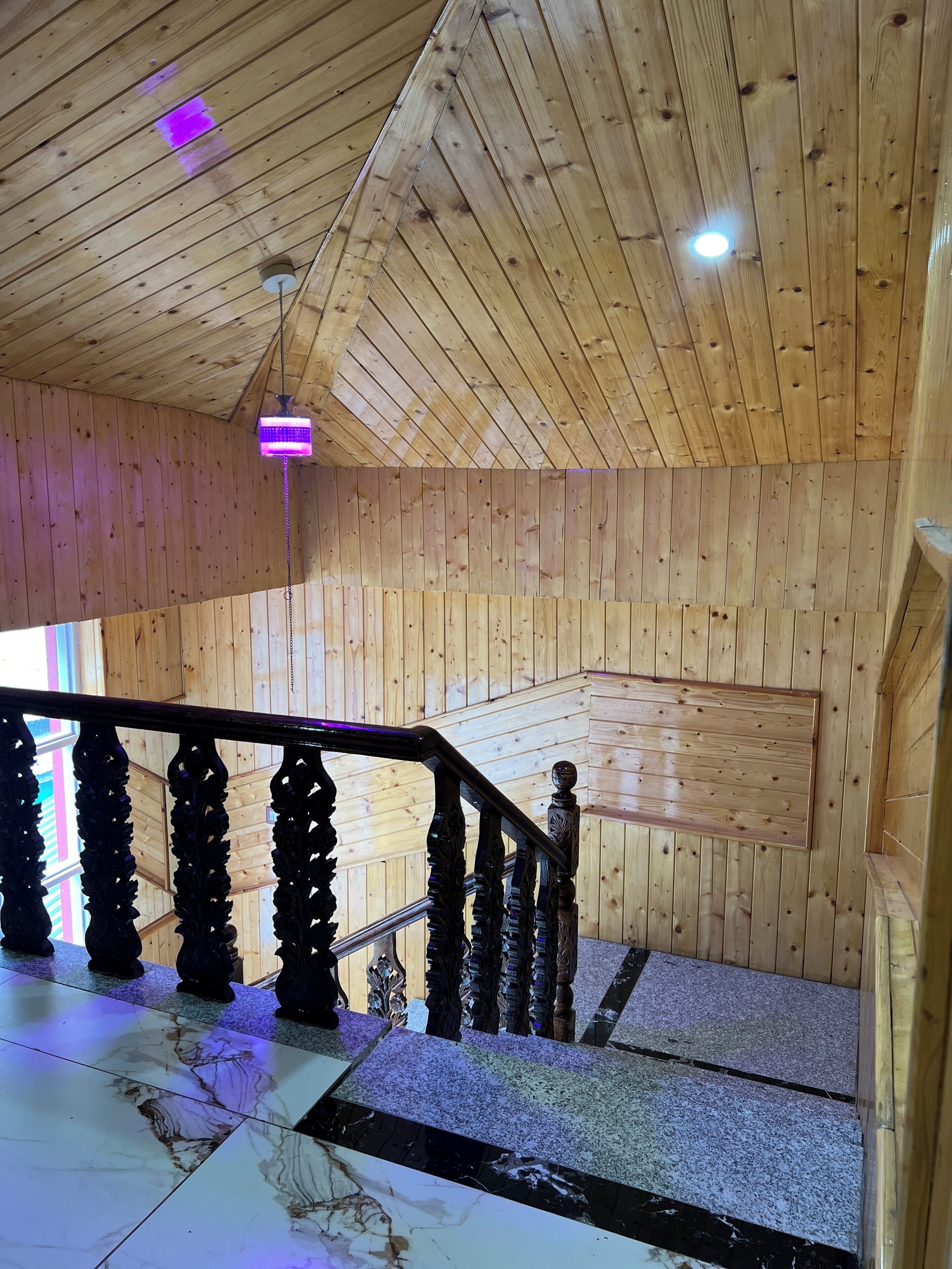 Interior de madera con una escalera, paredes de madera y una lámpara en el techo.
