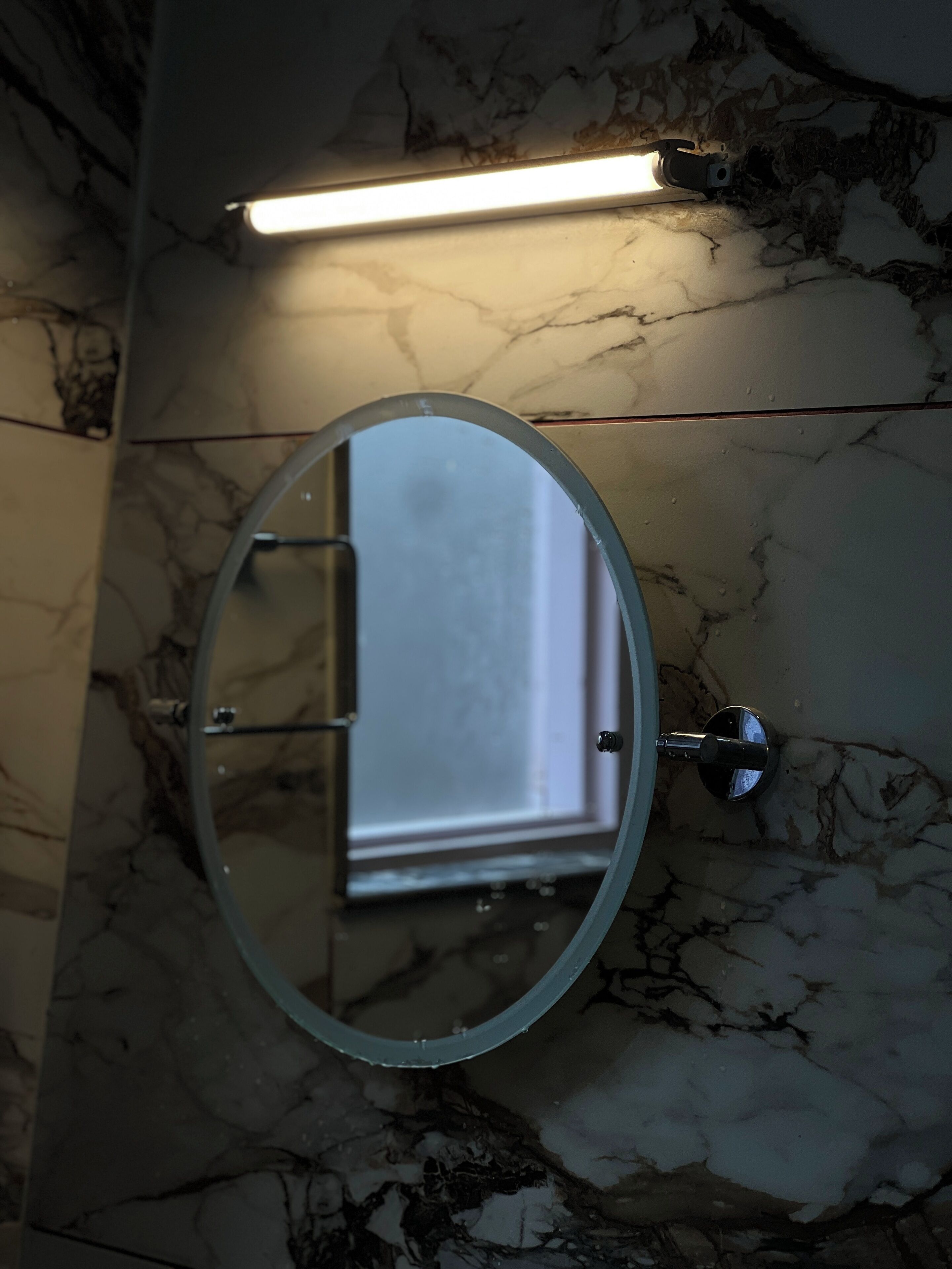 A bathroom with a marble floor, a round mirror, and a wall-mounted light fixture.