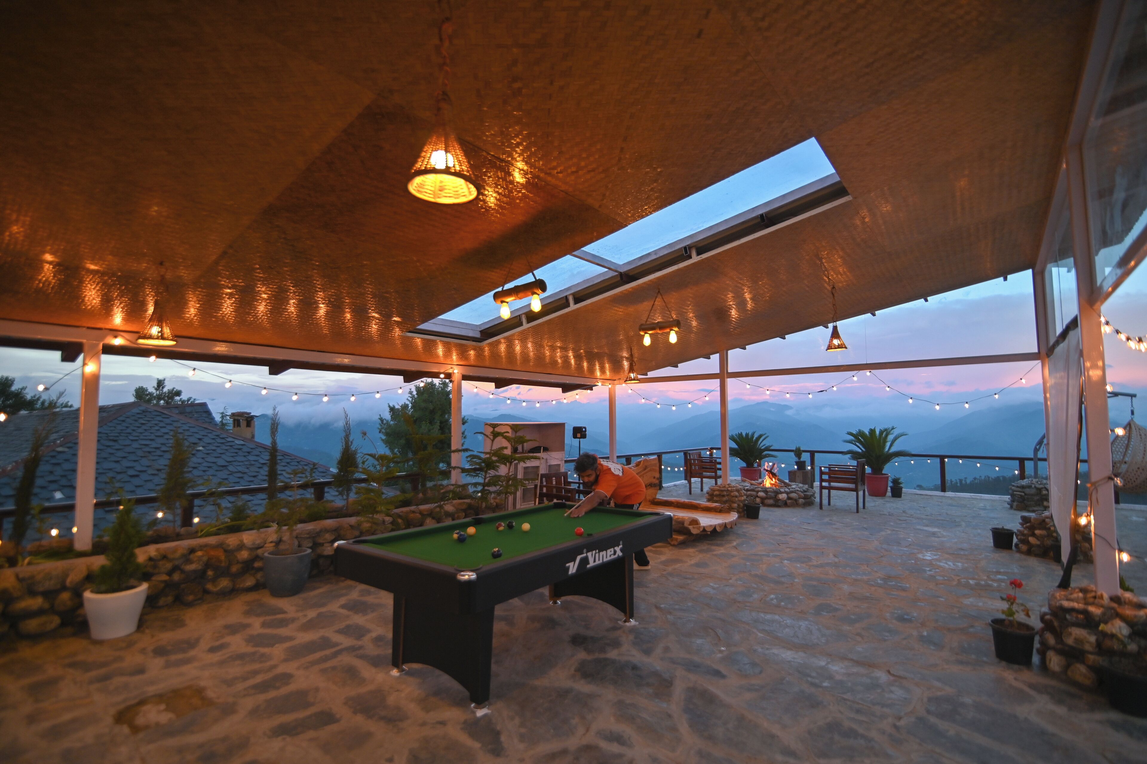 An outdoor pool table area with a stone floor, potted plants, and string lights.
