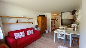 Un espacio habitable compacto con un sofá rojo, una pequeña mesa de comedor y una kitchenette.