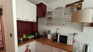 Una cocina compacta con armarios blancos, microondas, tetera y cafetera.