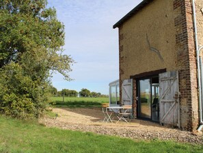 A rustic building with a large glass door, a wooden table and chairs outside, and a grassy field in the background. - Rural charm between Le Mans and Tours, renovated house in nature (Flée)