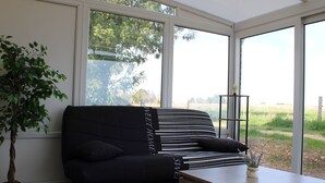 Una sala de estar moderna con un sofá negro, una mesa de centro de madera y un amplio ventanal con vistas a un campo verde.